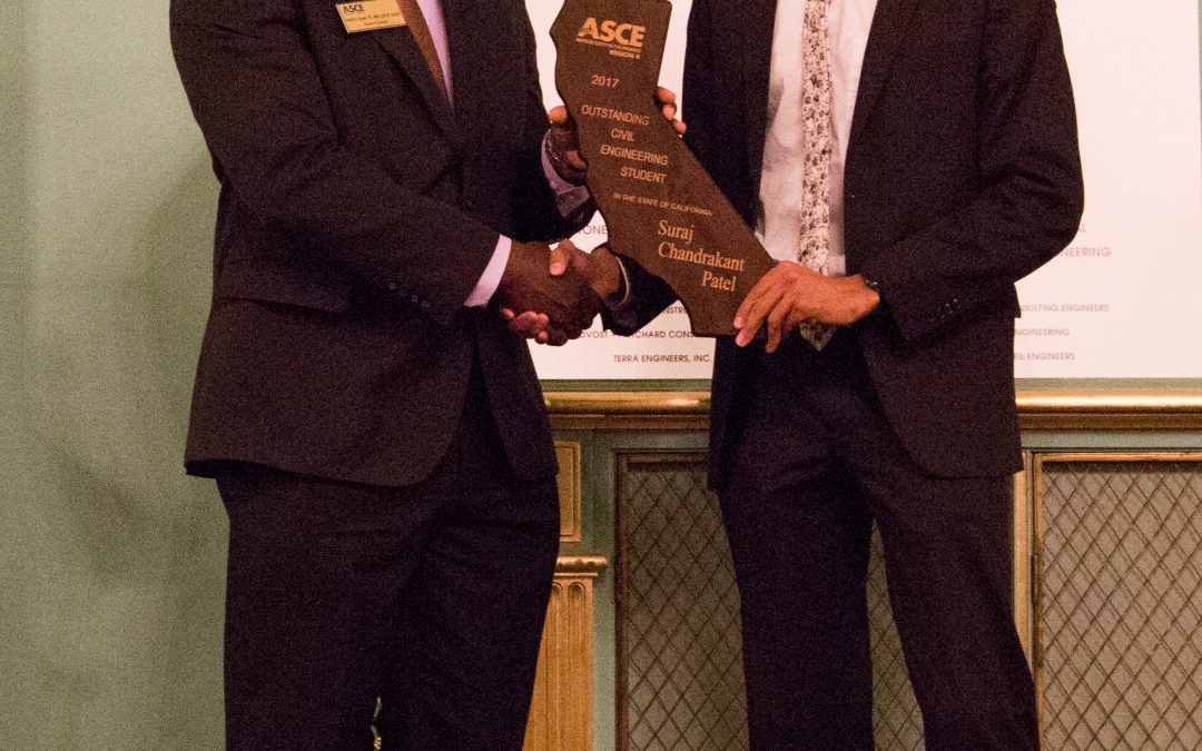 Man on right shakes hand with man on left while holding California-shaped wooden award that says "ASCE" next to their handshake. Both men are smiling and wearing formal suits