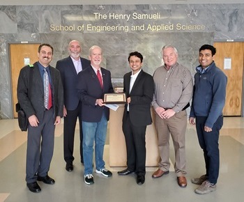Jeff Speck, the ESCSI Board Chairperson awarding certificate and $5,000 scholarship to Annesh Borthakur in center. also pictured are Dr. Sanjay Mohanty, Charles Kerzik from the Arcosa Lightweight, an ESCSI member in California, and Dr. Fariborz Tehrani, the ESCSI Director. wall of background reads "The Henry Samueli School of Engineering and Applied Science"